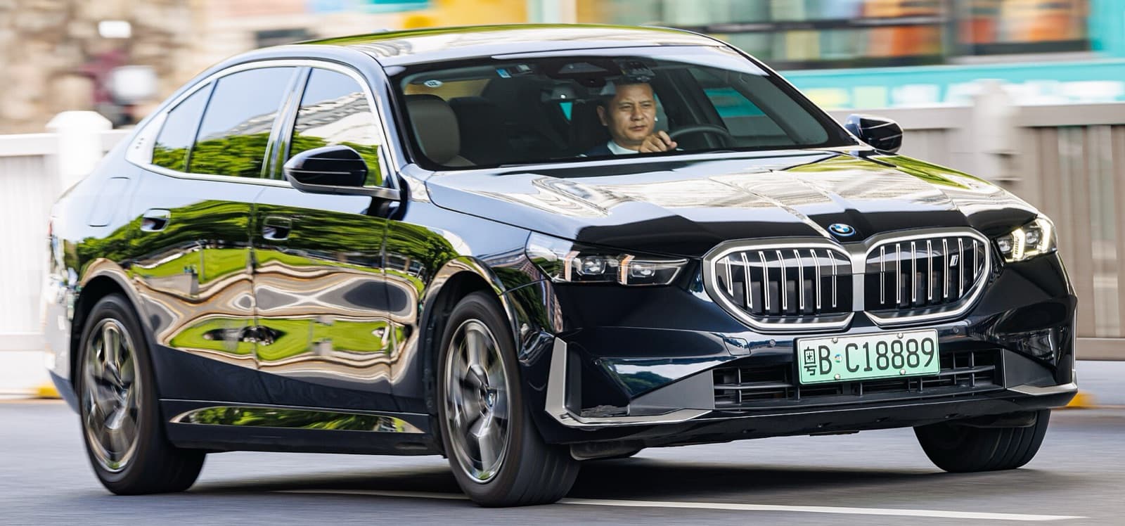 A dark blue BMW i5 electric sedan driving on a city street
