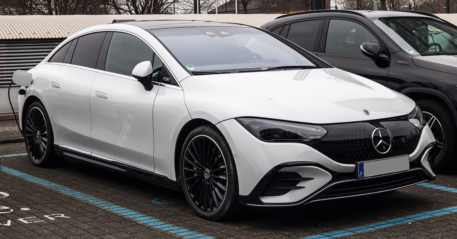 A white Mercedes-Benz EQE electric executive sedan parked at a charging bay